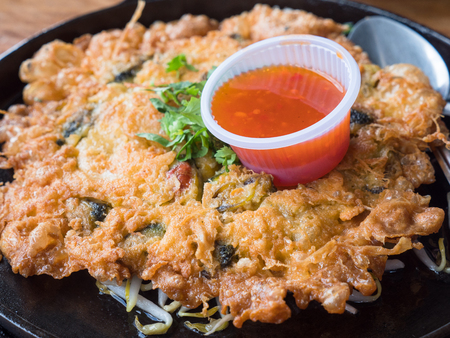 Hoy tod, a classic Thai course consisting of an omelet with mussels or oysters on a bed of bean sprouts served on an iron hot plate with chili sauce. Shallow depth of field with the nearest part in focus.の写真素材