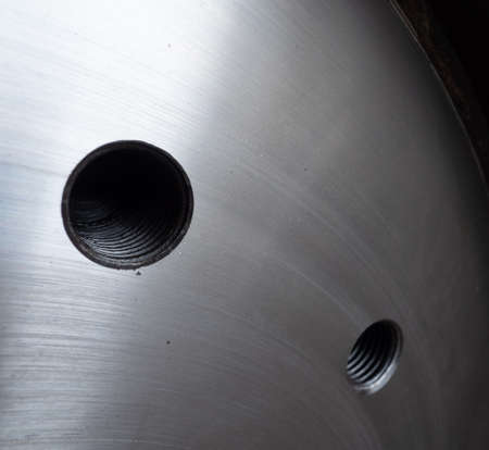 Stainless steel plate with threaded holes for bolts. Shallow depth of field with the nearest hole in...
