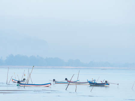 Mooring stakes and boats at dawn at a beach on the coast of Surat Thani province in Thailand.の写真素材