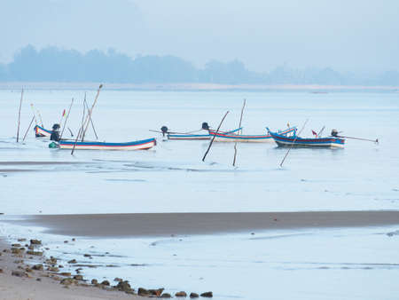 Mooring stakes and boats at dawn at a beach on the coast of Surat Thani province in Thailand.の写真素材