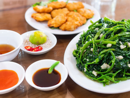 Vietnamese fried morning glory, rau muong xao toi, and Vietnamese fish cakes, cha ca quy nhon, out of focus in the background. Fried morning glory is a popular dish across large parts of Asia, made with watercress or water spinach, chili pepper, garlic and fish sauce, oyster sauce or soy sauce.の写真素材