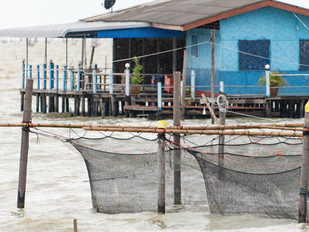 Fish farm at Songkhla Lake in Songkhla, south of Thailand on a rainy day. Shallow depth of field with the nets in the foreground in focus. Fisherman's shack in the background.の写真素材