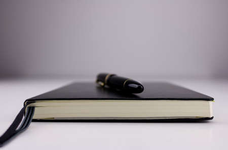 Low angle close up of a black fountain pen on top of a closed black notebook