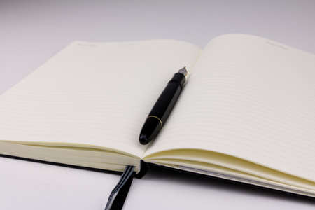 A black fountain pen on top of an open blank notebook