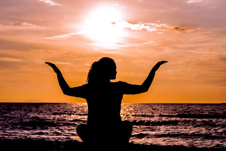 Female yoga lotos silhouette on beautiful beach during sunset. Tree Pose.の写真素材