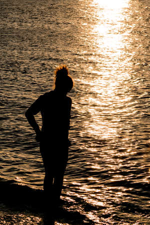 Silhouette of teenage girl on beautiful sea beach during sunsetの写真素材