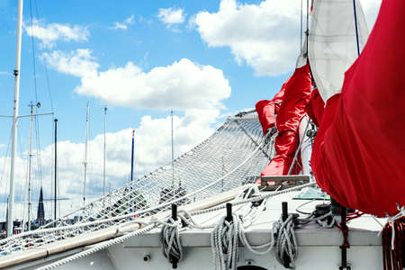 Details of bowsprit and gathered red sail of the tall ship on the cloudy sky background. Concepts:...