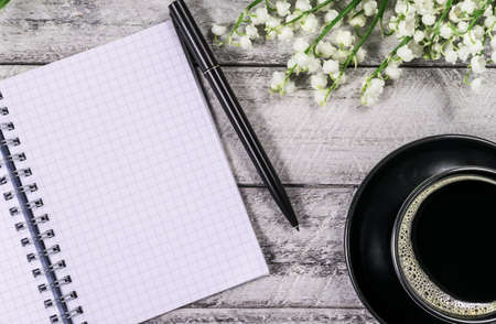 coffee cup, notebook, pen and  lily of the valleys on wooden background. top view copy space.の写真素材