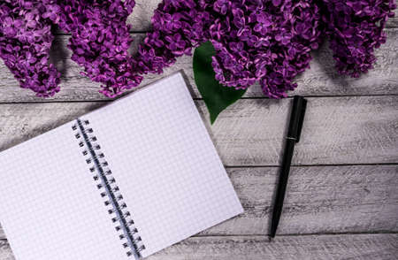 blank notebook, pen and lilac flowers on wooden background. top view copy space.の写真素材