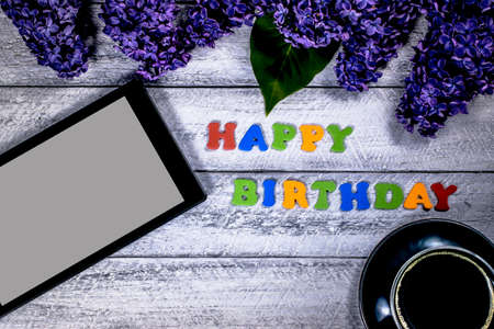 happy birthday concept with top view and copy space.  lilac flowers, tablet  and coffee cup on...