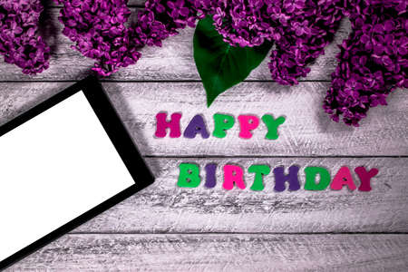 happy birthday concept with top view and copy space.  lilac flowers and tablet on wooden background.の写真素材