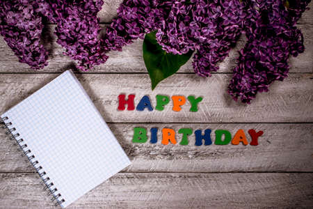 happy birthday concept with top view and copy space.  lilac flowers and notebook on wooden background.の写真素材
