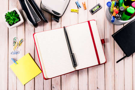 Top view workspace mockup on wooden background with blank notebook with copy space, pen, tacker, punch, clips and accessories. Overhead view. Flat lay, top viewの写真素材
