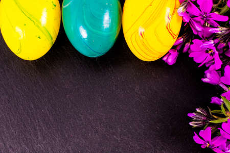 close-up of colorful easter eggs and phlox flowers on stone background with copy space. border...