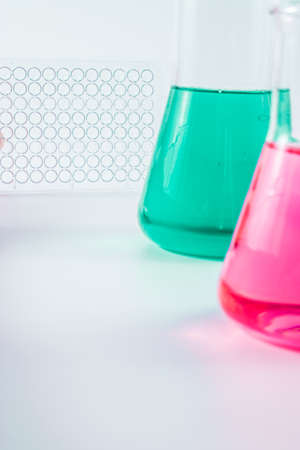 Research, science and clinic background. 96 well micro plate and laboratory beakers with colorful liquids and reagents.の写真素材
