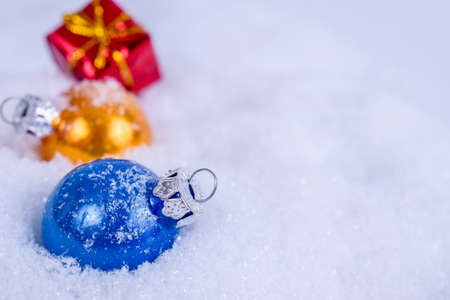Close-up of colorful xmas balls and red gift under snowflakes in snow. Christmas and New Year concept with copy space. Christmas greeting card.の写真素材