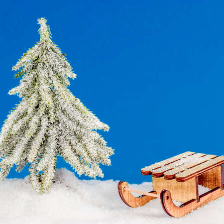 Christmas tree in snow under snowflakes with sledge and red xmas gifts on blue background. Christmas and New Year concept. Christmas greeting card.の写真素材