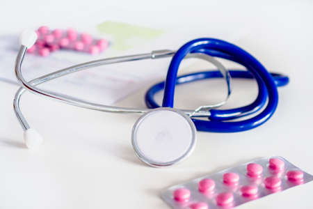 blue stethoscope and pink pills on white table in doctors office or in hospital.の写真素材