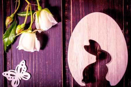 easter rabbit and egg with white rose flowers close-up and butterfly on dark wooden background with...