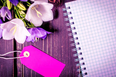 Spring flowers close-up with blank note book, copy space and pink sale label on wooden background. Spring summer border template. mock-up floral background. sale, greeting and celebration cardの写真素材
