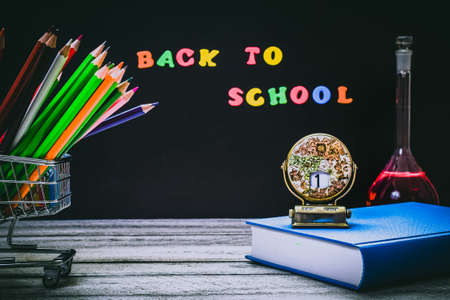 Back to School and Education concept. shopping cart with color pencils, book with red apple and calendar on chalkboard background. school border with copy spaceの写真素材