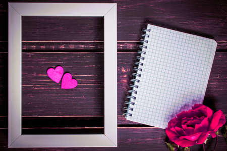 blank photo frame with two hearts , blank notebook with copyspace and pink rose flowers on wooden background. greeting card and holiday concept.の写真素材