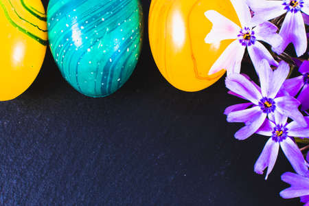 close-up of colorful easter eggs and phlox flowers on stone background with copy space.