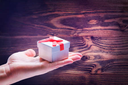 hand holds gift in hand. woman holding gift box over wooden background. magic gift with red bow. Christmas or Xmas scene. birthday or romantic congratulation card. template and border with free spaceの写真素材