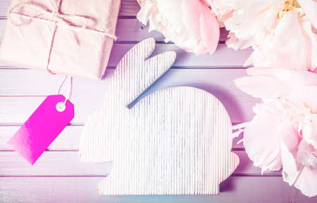 easter rabbit with peonies flowers close-up, gift box and sale label or tag on wooden background with copy space. easter mock-up template. easter sale, greeting and celebration card concept.の写真素材