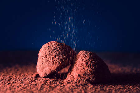 Chocolate truffles and falling cocoa powder on blue background, macro. delicious homemade truffle with dark chocolate.の写真素材