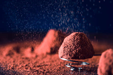 Chocolate truffles and falling cocoa powder on blue background, macro. delicious homemade truffle with dark chocolate.の写真素材
