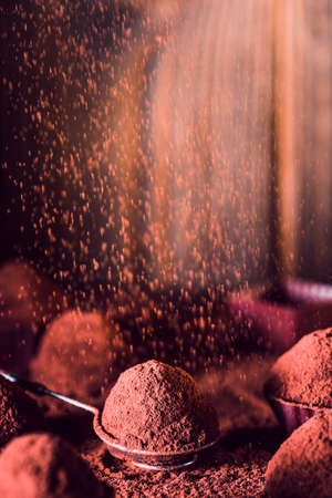 Chocolate truffles and falling cocoa powder on wooden background, macro. delicious homemade truffle with dark chocolate.の写真素材