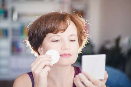 Woman applying makeup applicator and looking at mirror. girl makes makeupの写真素材