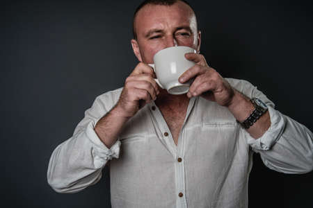 bearded man holding white coffee cup. man with morning coffee in studio on grey backgroundの写真素材