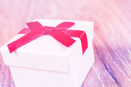 white paper gift box with thin red ribbon bow on old wood table, with copy spaceの写真素材