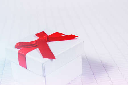 white paper gift box with thin red ribbon bow on old wood table, with copy spaceの写真素材