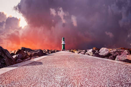 Pathway to Lighthouse on the sea under dramatic fire sky