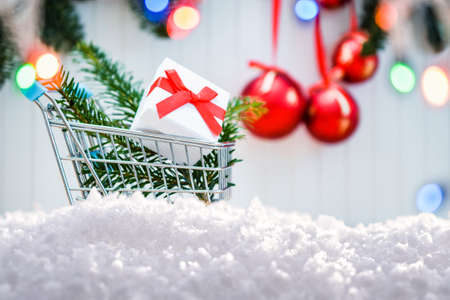 Happy Christmas. Christmas shopping concept. Shopping cart with gift box. red christmas balls with fir tree branches and snow frame. Xmas greeting card and border with copy spaceの写真素材