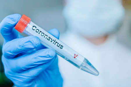 Nurse in a respiratory protective mask and labotator gloves holds a test tube with a positive...