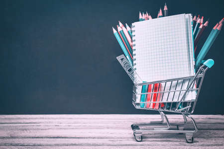 Back to School and Education concept. shopping cart with supplies, notebook and colorful pencils on chalkboard background. school border with copy spaceの写真素材