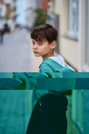 teenager boy in hoodie and leather jacket walks away on the city street and turns around.の写真素材