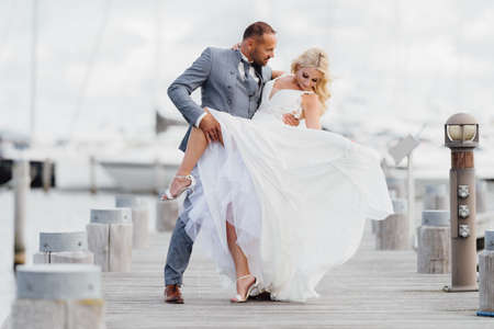 Happy just married couple dancing on the beach with yachts in the background. Wedding by the sea on the beachの写真素材