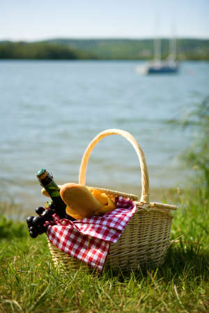 Picnic basket with food and cider bottle near the waterの写真素材