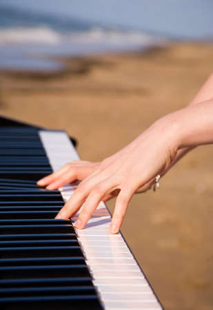 Playing music at the seashore. Beautiful female hands, piano keyboard and ocean or sea in the backgroundの写真素材