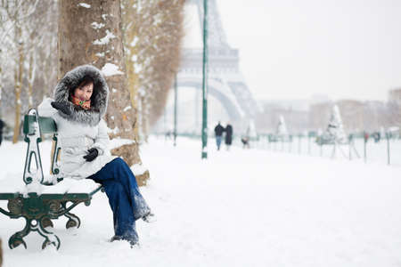 Beautiful girl in fur hood sitting on a bench near the Eiffel towerの写真素材