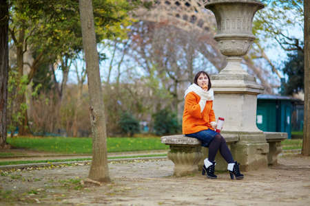 Young woman in Paris with take-away coffee and pastry, having a picnic near the Eiffel towerの写真素材