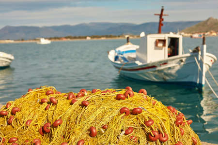 Pile of yellow fishing nets in port with boats in the background. Focus on fishing nets. Nafplion, Greeceの写真素材