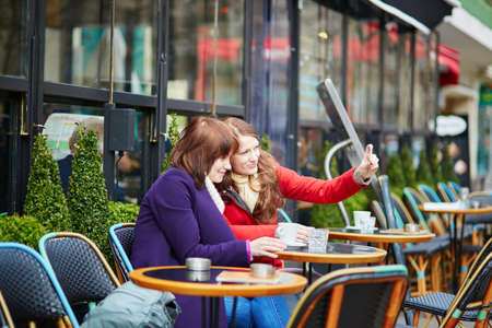 Two cheerful girls making self picture (selfie) in a Parisian street cafeの写真素材