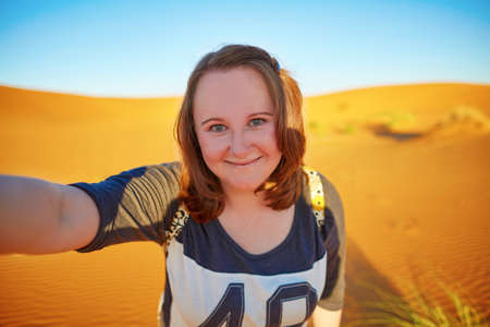Happy smiling tourist taking selfie with sand dunes in Sahara desert, at Erg Chebby, Merzouga,...