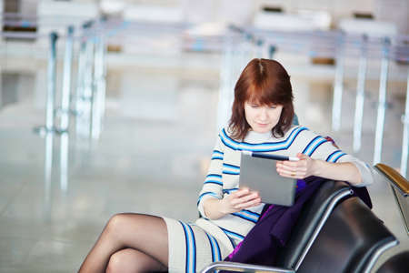 Young female passenger at the airport, using her tablet computer while waiting for her flightの写真素材